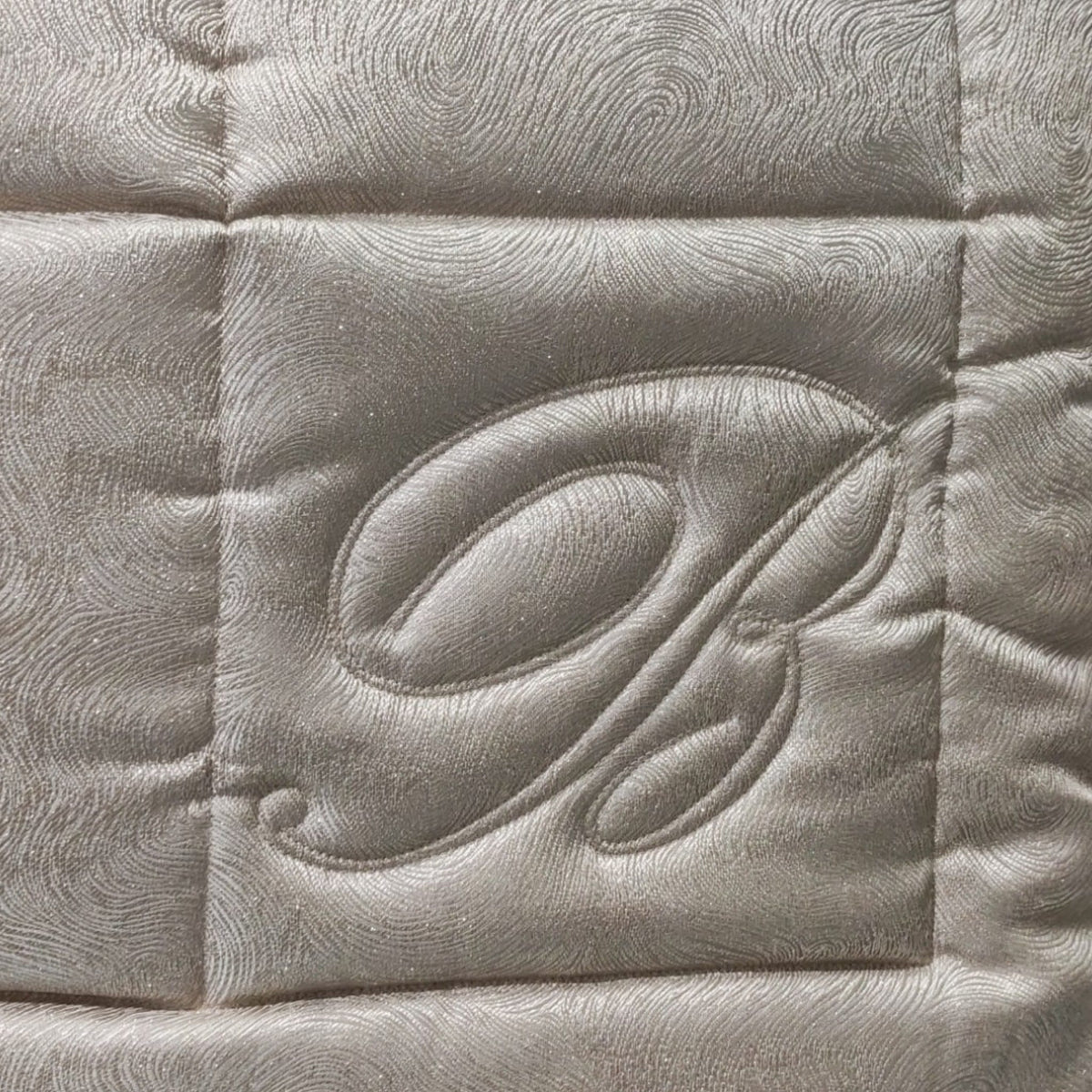 Dettaglio della trapunta Sfumature Blumarine Home con monogramma B in rilievo e motivo a onde