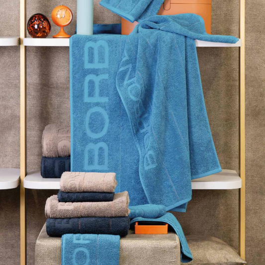 Asciugamani Borbonese Home Gessato Spugna in cotone, ambientati in bagno con logo cesellato e colori assortiti.