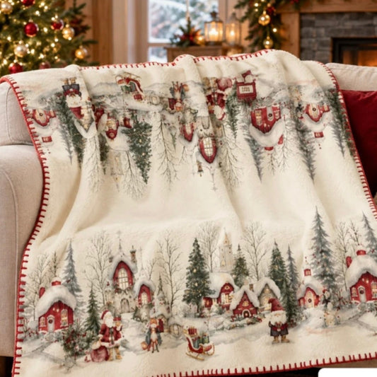 Plaid natalizio Magic Forest con casette innevate e abeti, disteso su un divano accanto all'albero di Natale.