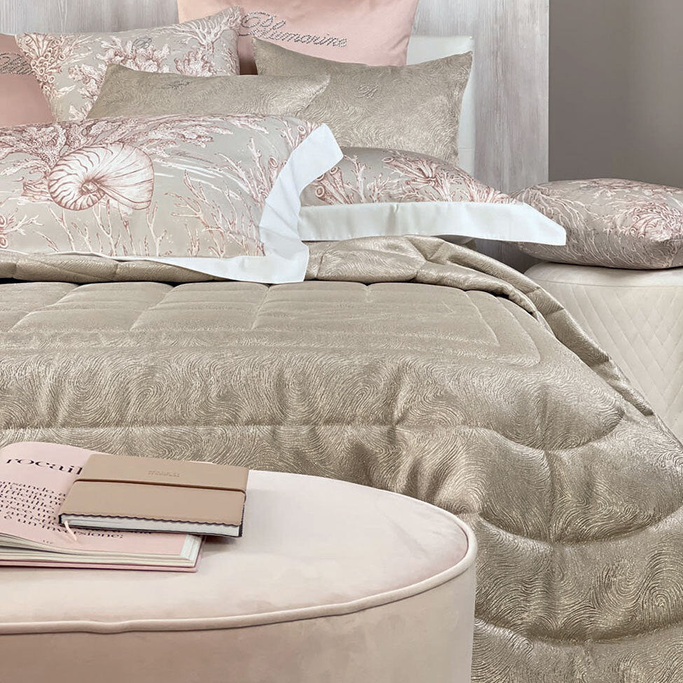 Trapunta Sfumature Blumarine Home ambientata sul letto con motivo a onde e cuscini decorativi
